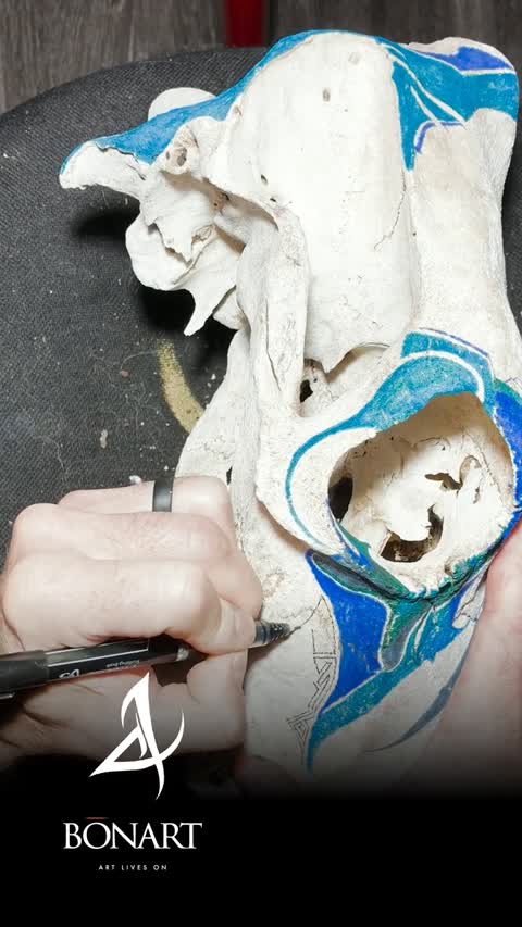 Joel’s hand drawing fine details on a blue and cream animal skull